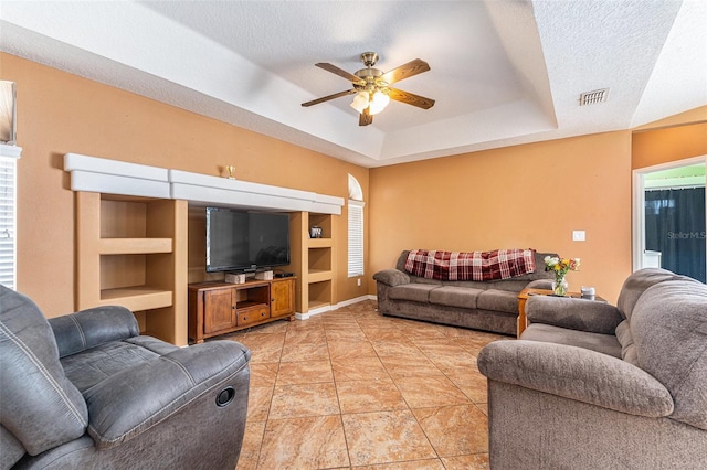 living room with light tile patterned flooring, ceiling fan, a raised ceiling, and a textured ceiling