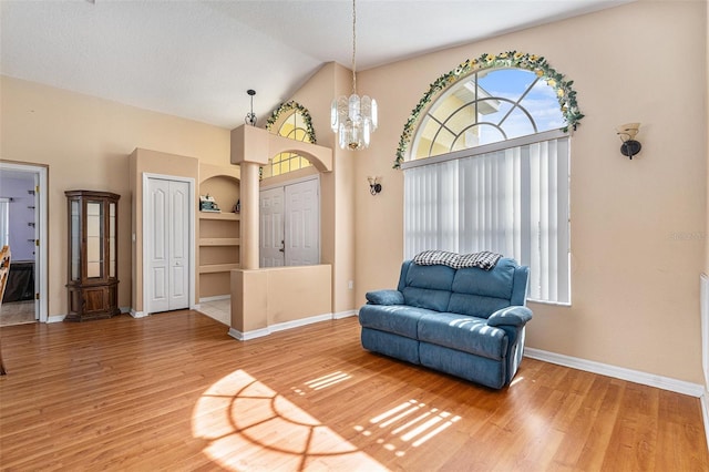 living area featuring high vaulted ceiling, hardwood / wood-style floors, an inviting chandelier, and built in shelves