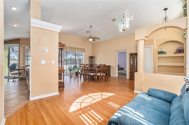 living room featuring ceiling fan with notable chandelier, hardwood / wood-style floors, vaulted ceiling, and built in features