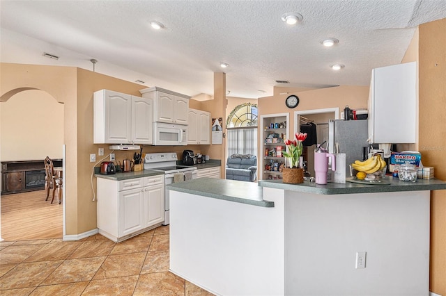 kitchen with light tile patterned flooring, white cabinets, white appliances, kitchen peninsula, and a textured ceiling