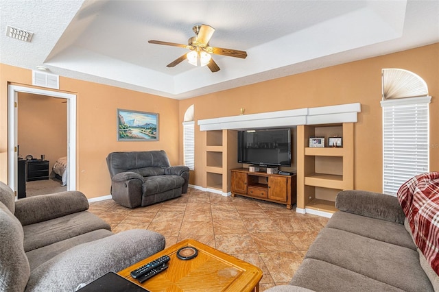 living room with a tray ceiling, a textured ceiling, and ceiling fan