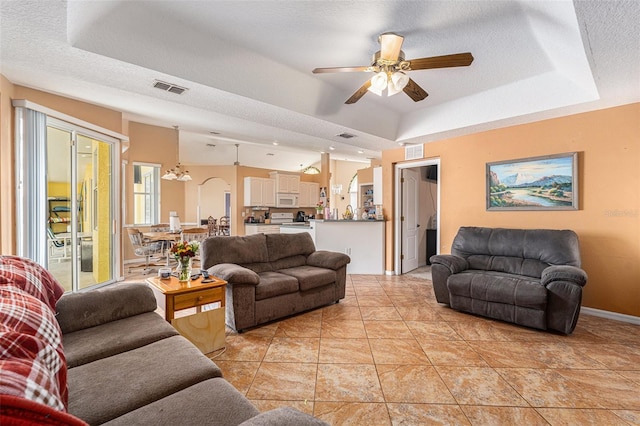 living room with ceiling fan, a tray ceiling, and a textured ceiling