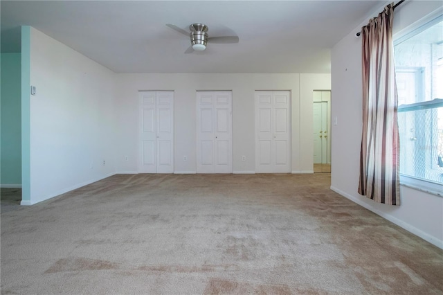 unfurnished bedroom featuring two closets, light colored carpet, and ceiling fan