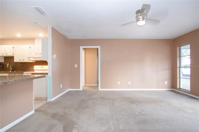 unfurnished living room featuring sink, light colored carpet, and ceiling fan