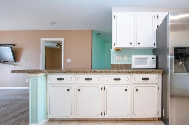 kitchen featuring kitchen peninsula, stainless steel fridge, dark stone counters, white cabinets, and light colored carpet