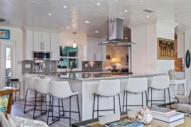 kitchen featuring island range hood, white cabinets, light stone countertops, and hardwood / wood-style flooring