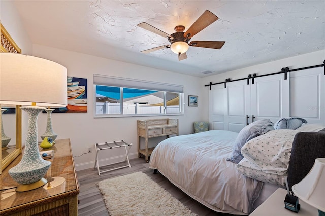 bedroom with wood-type flooring, a barn door, a closet, and ceiling fan