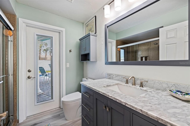 bathroom with hardwood / wood-style floors, vanity, a shower with shower door, and toilet