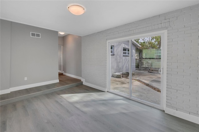 spare room with hardwood / wood-style floors and brick wall