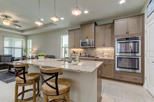 kitchen featuring light stone counters, appliances with stainless steel finishes, decorative light fixtures, a kitchen bar, and an island with sink