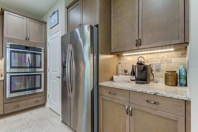 kitchen with backsplash, light tile patterned floors, light stone counters, and appliances with stainless steel finishes