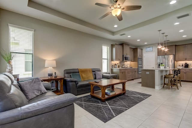 living room with light tile patterned flooring, ceiling fan, a raised ceiling, and sink