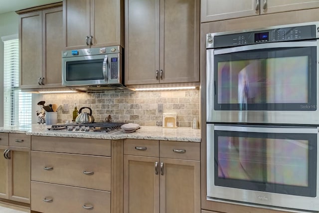 kitchen with tasteful backsplash, light stone countertops, and appliances with stainless steel finishes