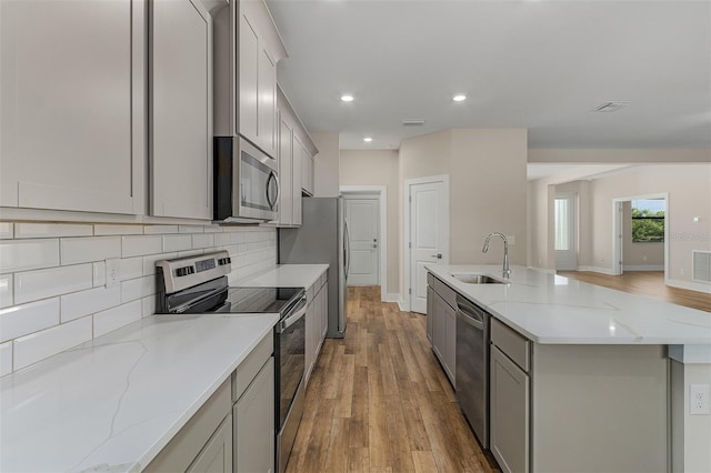 kitchen with sink, light stone counters, stainless steel appliances, and light wood-type flooring