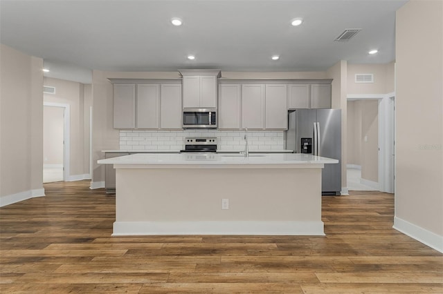 kitchen featuring a kitchen island with sink, light hardwood / wood-style flooring, sink, gray cabinets, and stainless steel appliances