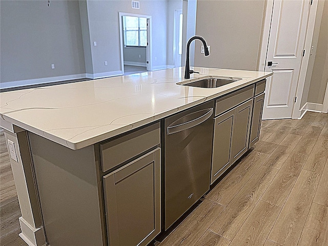 kitchen featuring stainless steel dishwasher, light stone countertops, sink, and a center island with sink