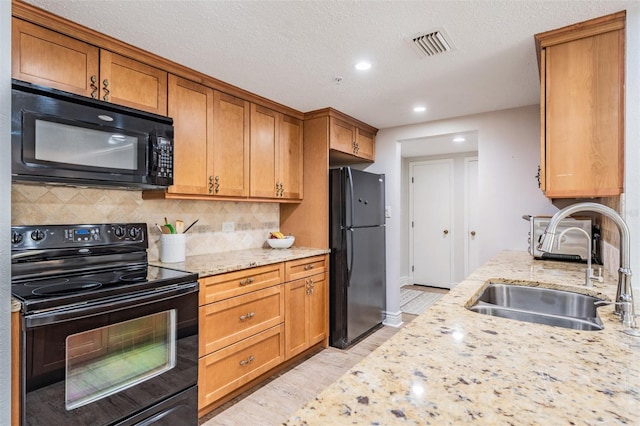 kitchen with tasteful backsplash, light stone countertops, light wood-type flooring, black appliances, and sink