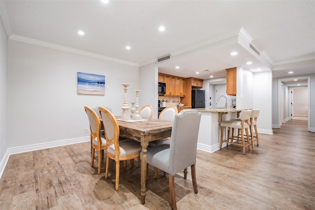 dining room with sink, crown molding, and light wood-type flooring