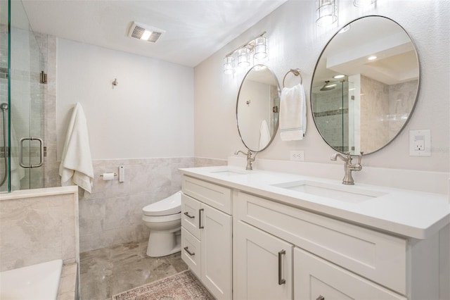 bathroom featuring a shower with door, vanity, toilet, and tile walls