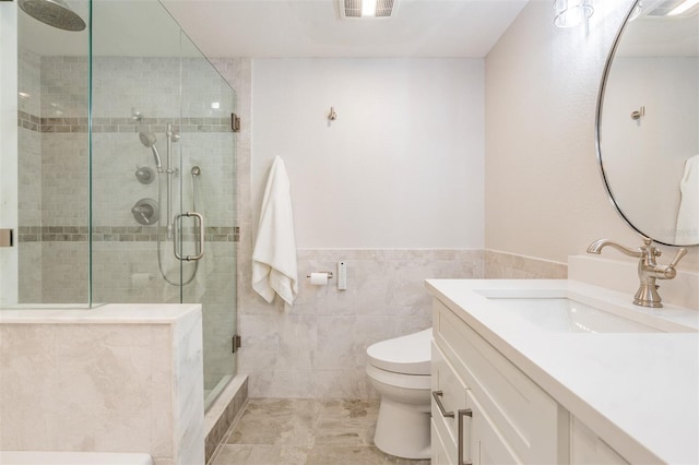 bathroom with tile walls, vanity, a shower with shower door, and toilet