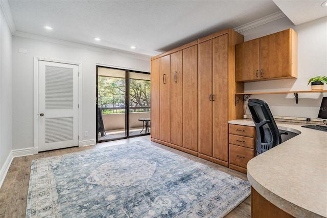 home office with built in desk, ornamental molding, light hardwood / wood-style flooring, and a textured ceiling