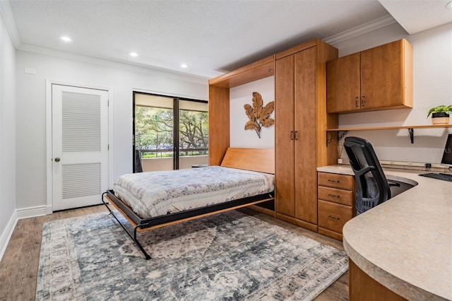 bedroom with built in desk, crown molding, hardwood / wood-style flooring, and access to outside