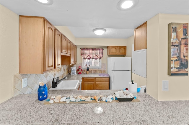 kitchen with backsplash, light stone countertops, sink, and white refrigerator