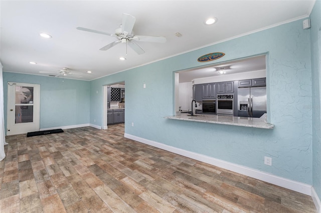 unfurnished living room featuring ceiling fan, hardwood / wood-style flooring, ornamental molding, and sink