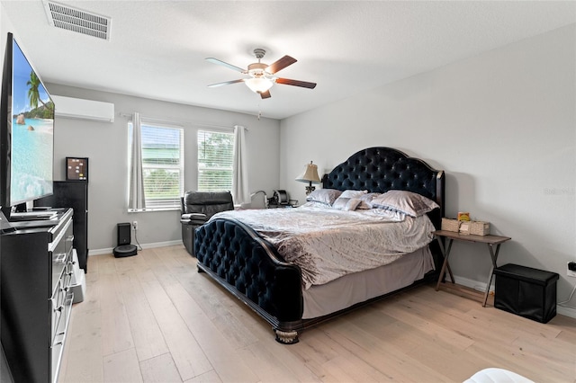 bedroom with a wall unit AC, light wood-type flooring, and ceiling fan