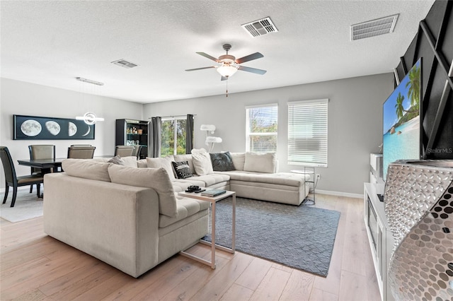 living room featuring ceiling fan, a textured ceiling, and light hardwood / wood-style flooring