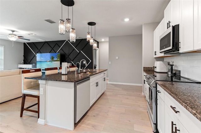 kitchen featuring white cabinetry, a kitchen island with sink, stainless steel appliances, and decorative light fixtures