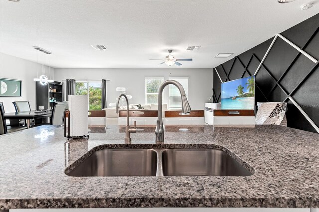 kitchen with stone counters, a textured ceiling, sink, and hanging light fixtures