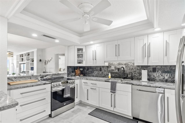 kitchen with a raised ceiling, sink, white cabinetry, light stone counters, and stainless steel appliances