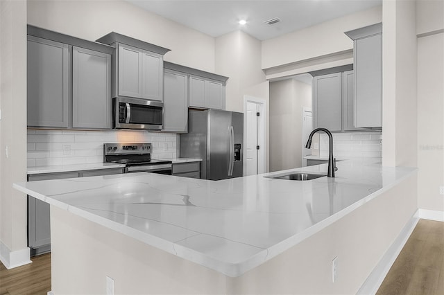 kitchen featuring stainless steel appliances, kitchen peninsula, and gray cabinetry