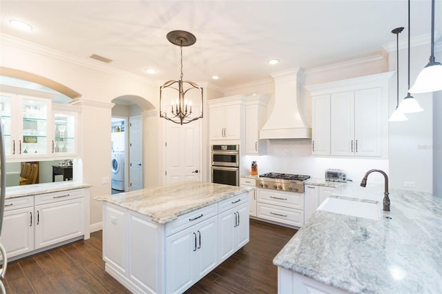 kitchen featuring sink, decorative light fixtures, custom range hood, and white cabinets