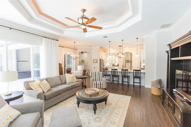 living room with dark hardwood / wood-style flooring, ceiling fan with notable chandelier, ornamental molding, and a raised ceiling