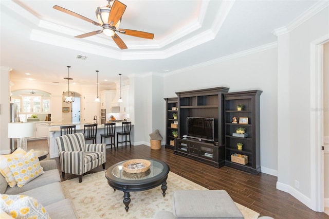 living room featuring ceiling fan, dark hardwood / wood-style floors, a tray ceiling, and ornamental molding