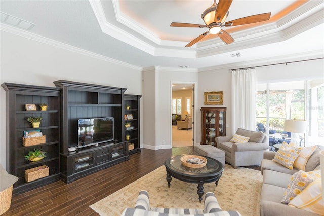 living room with dark wood-type flooring, ceiling fan, a raised ceiling, and crown molding