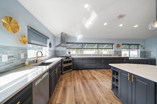 kitchen featuring sink, hanging light fixtures, light stone countertops, stainless steel appliances, and wall chimney exhaust hood