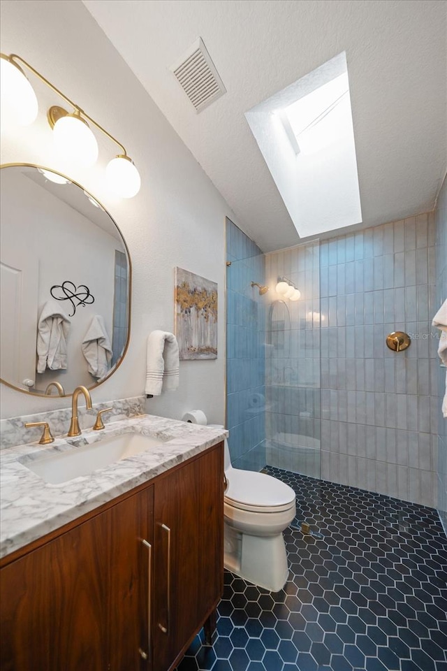 bathroom with toilet, vanity, tile patterned floors, tiled shower, and a skylight