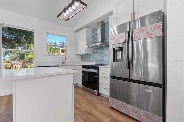 kitchen featuring appliances with stainless steel finishes, wall chimney exhaust hood, vaulted ceiling, white cabinets, and a kitchen island