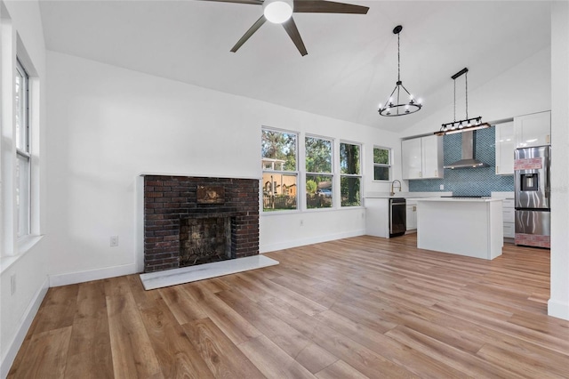 unfurnished living room featuring light wood-type flooring, a brick fireplace, ceiling fan with notable chandelier, vaulted ceiling, and sink