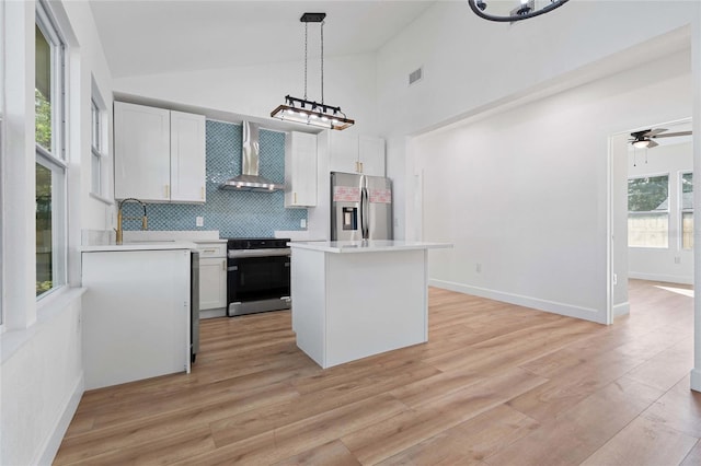 kitchen featuring pendant lighting, white cabinets, wall chimney range hood, and stainless steel appliances