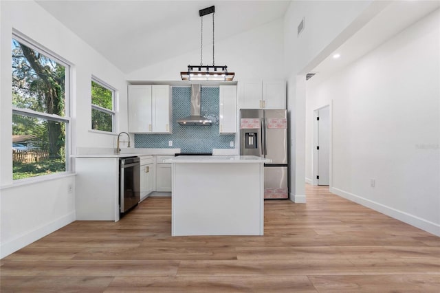 kitchen with pendant lighting, white cabinets, wall chimney range hood, tasteful backsplash, and stainless steel appliances