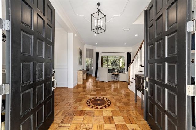 foyer entrance with ornamental molding, a chandelier, and light parquet flooring