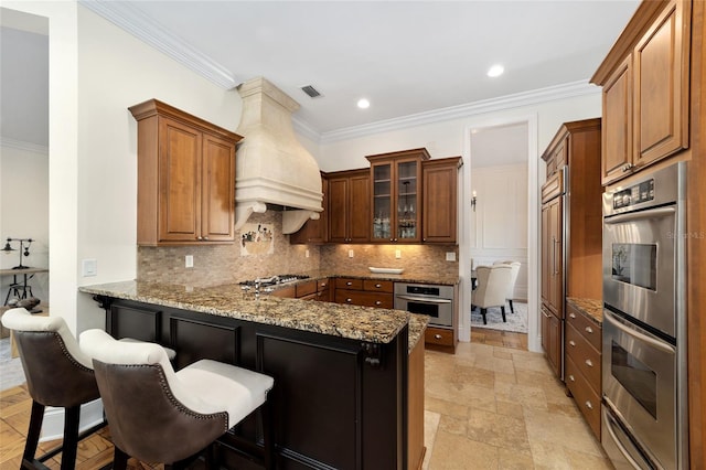 kitchen featuring appliances with stainless steel finishes, kitchen peninsula, custom exhaust hood, light stone counters, and ornamental molding