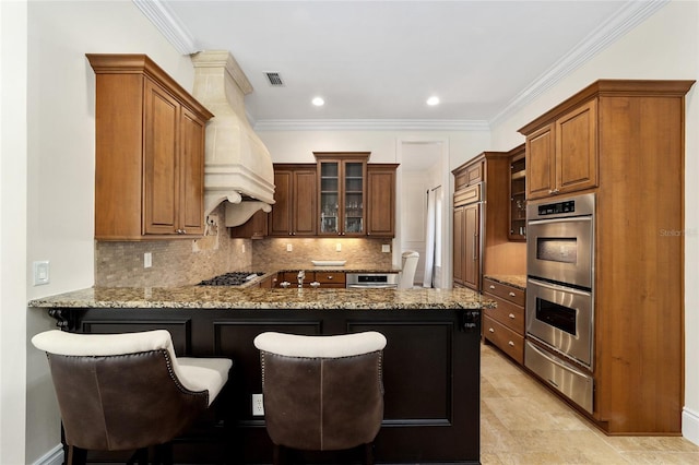 kitchen with appliances with stainless steel finishes, kitchen peninsula, light stone counters, and a kitchen bar