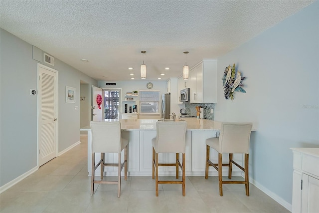 kitchen with a kitchen bar, kitchen peninsula, appliances with stainless steel finishes, pendant lighting, and white cabinetry