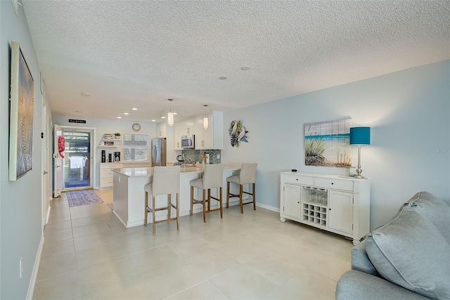 kitchen featuring stainless steel appliances, kitchen peninsula, a textured ceiling, a breakfast bar area, and white cabinets