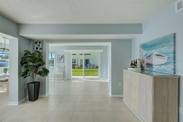 hall with a healthy amount of sunlight, light tile patterned floors, and a textured ceiling